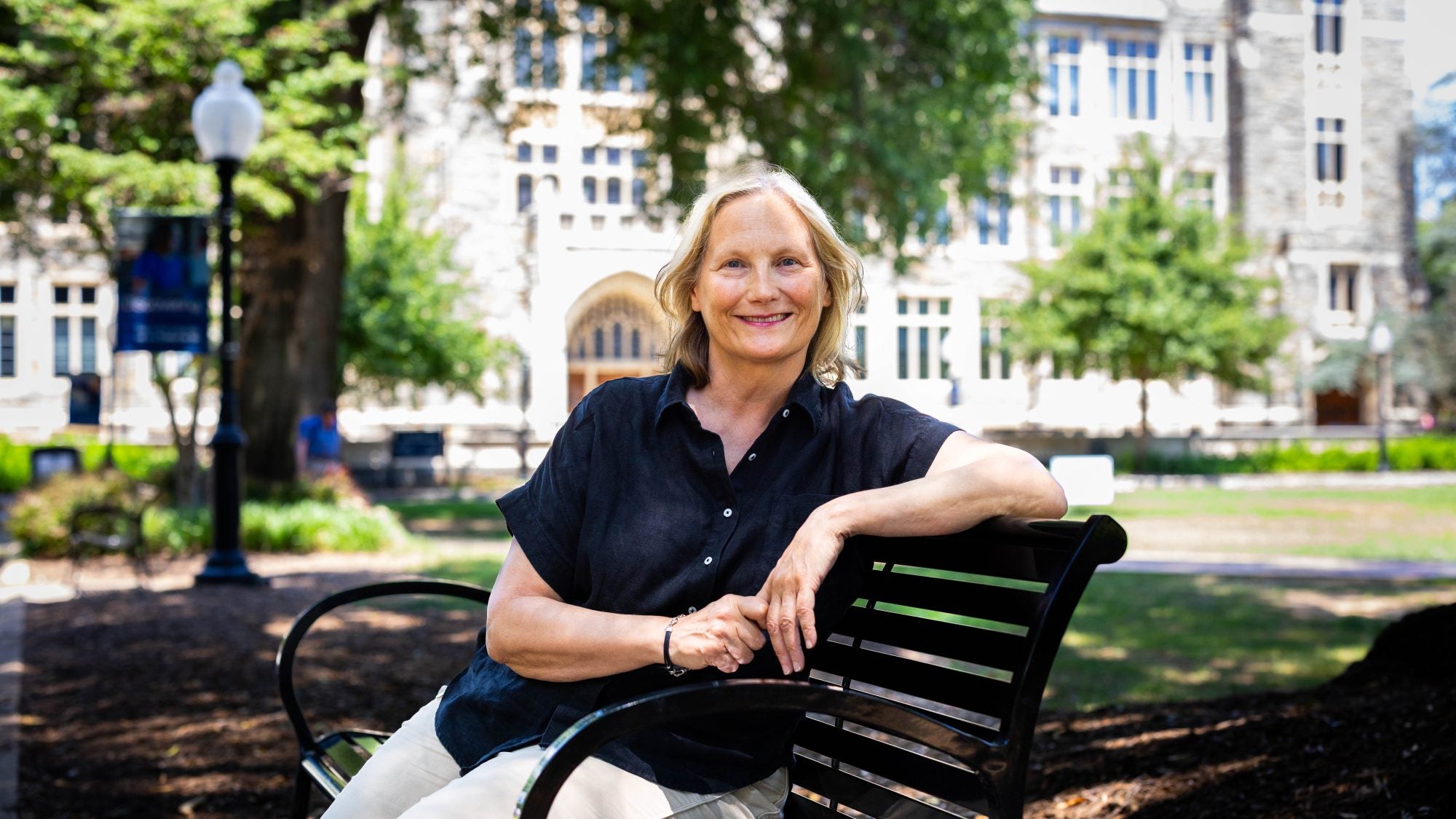 A blonde woman in a navy shirt smiles on a bench