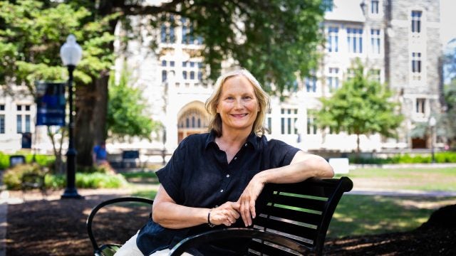 A blonde woman in a navy shirt smiles on a bench