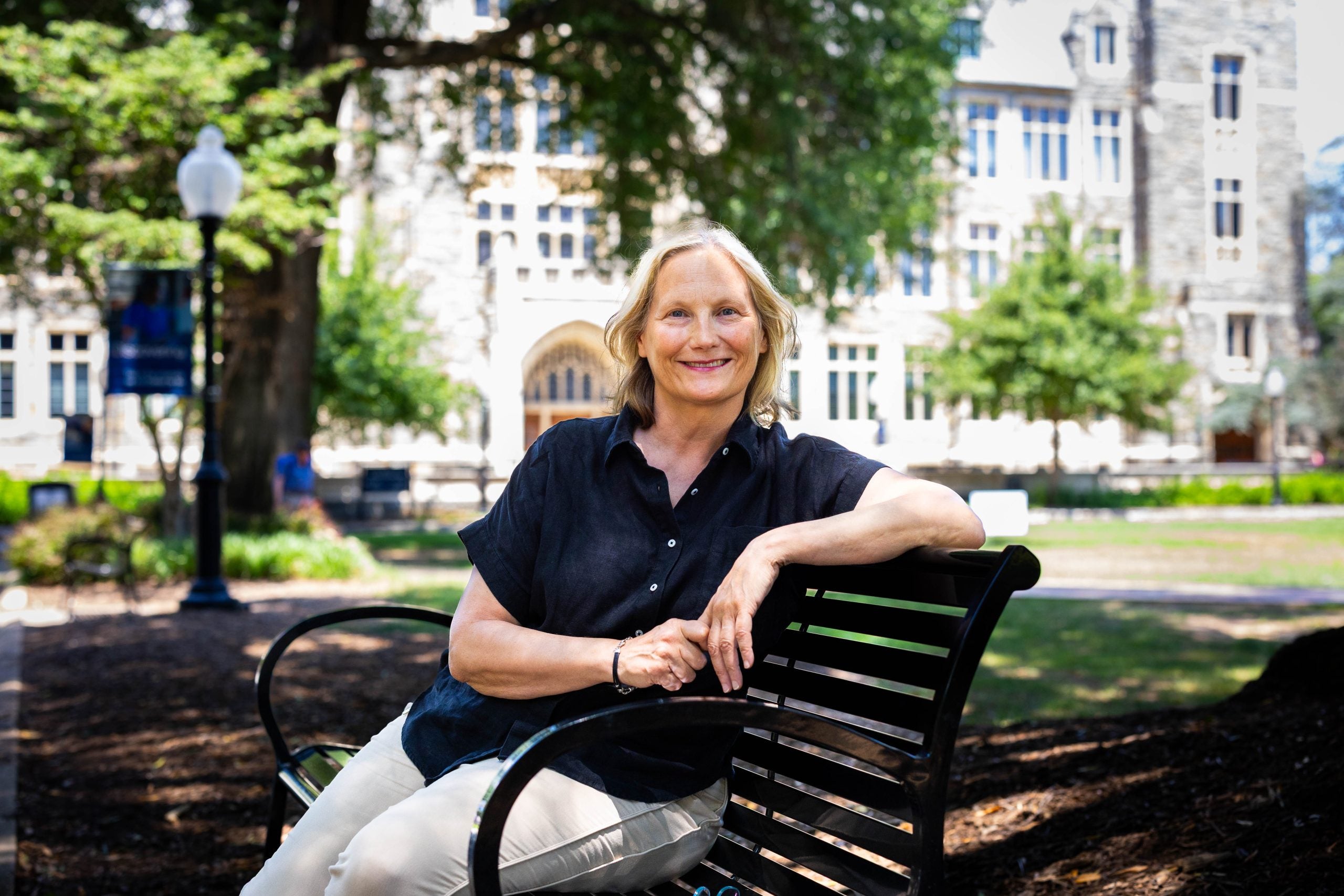 A blonde woman in a navy shirt smiles on a bench