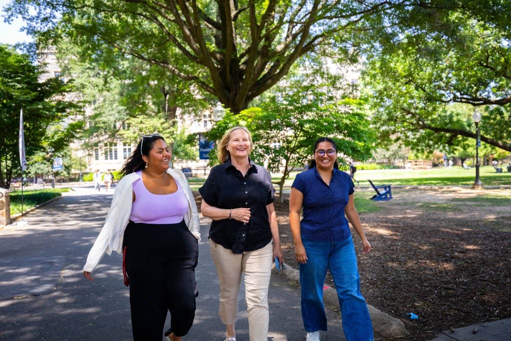 A woman links arms with two others while walking on a college campus