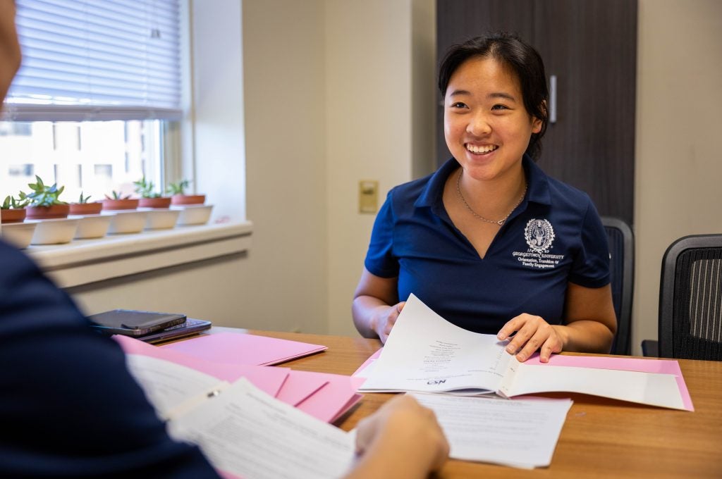 A student in a blue polo smiles while leafing through papers