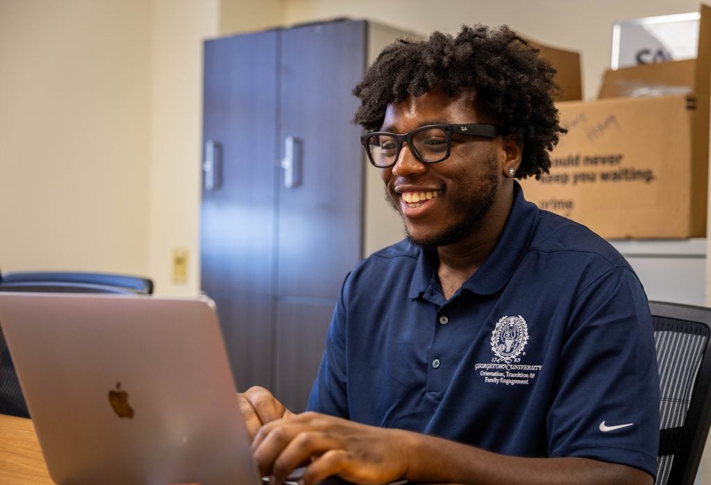 A student smiles while typing on a laptop
