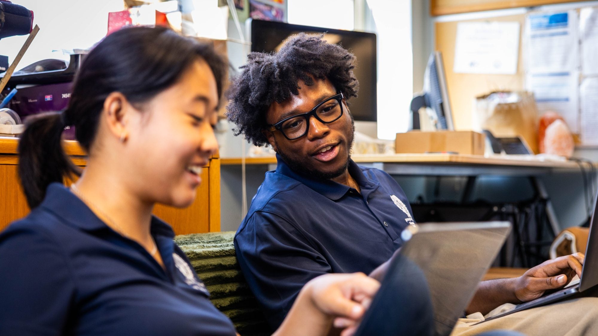 Two students smile while looking at a laptop