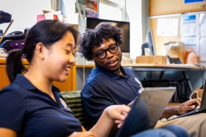 Two students smile while looking at a laptop