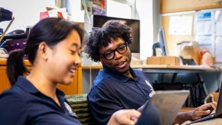 Two students smile while looking at a laptop