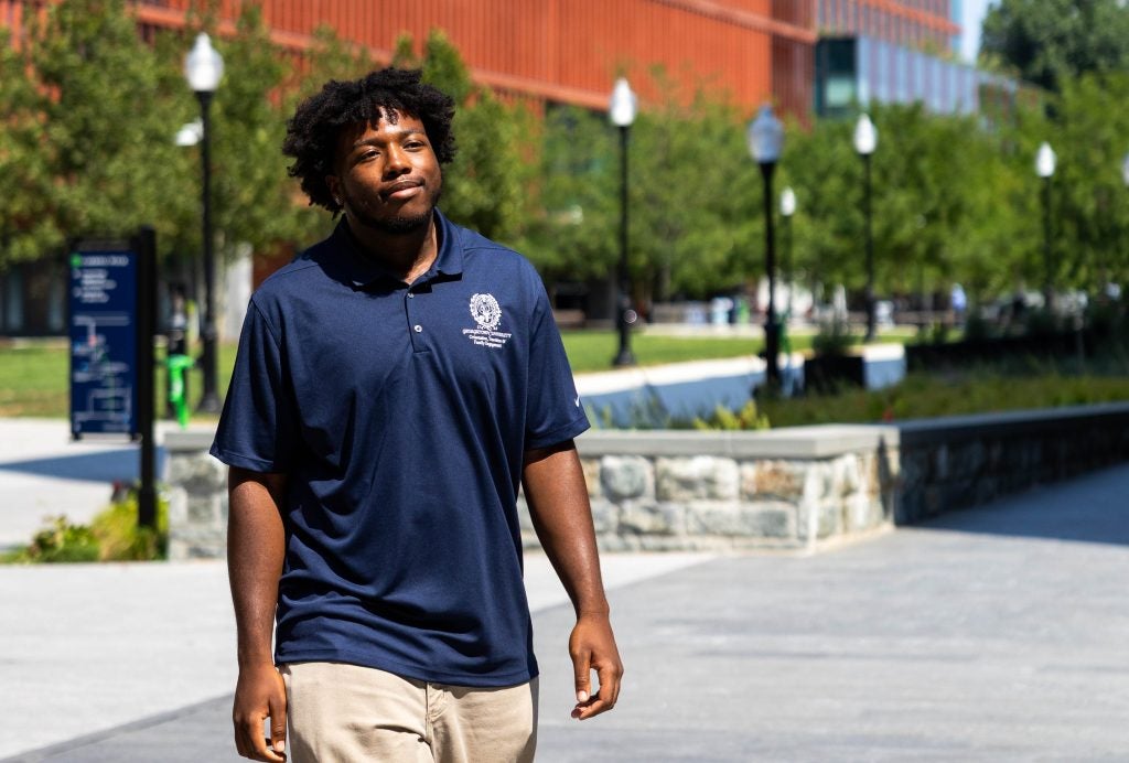 A male student wearing a blue polo walks outside on a sunny day