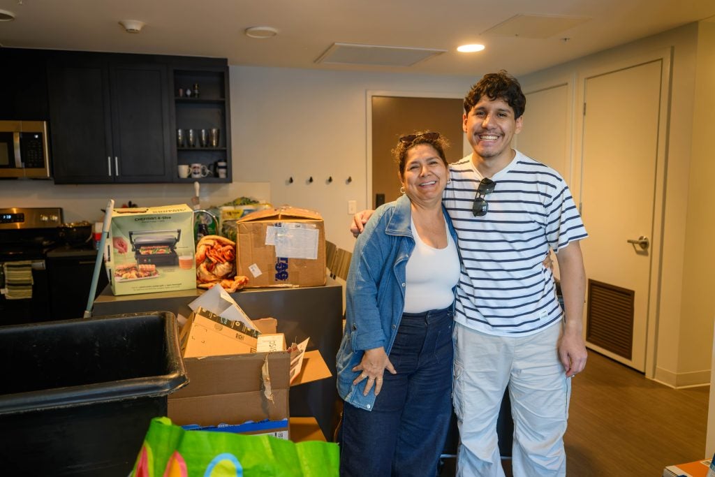 Young Hispanic man with his mother smiling while moving into an apartment
