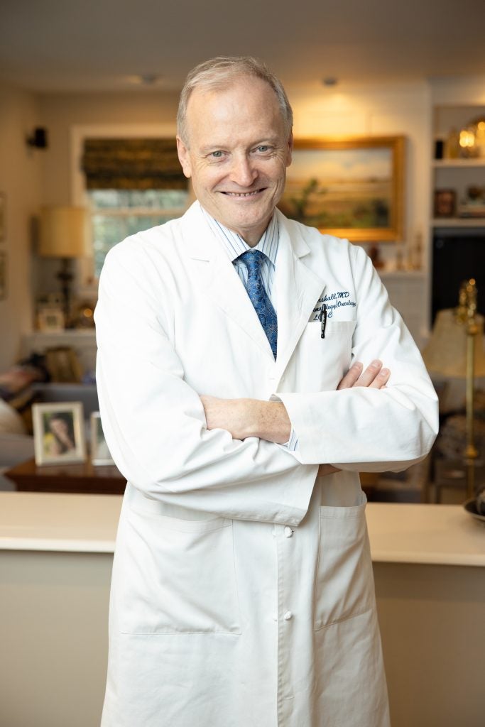 Older Caucasian man smiling in doctor's white coat with arms crossed
