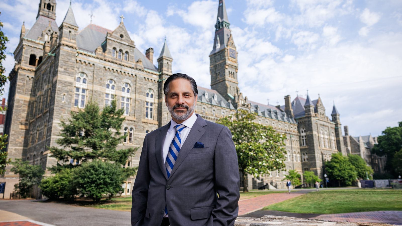 Eduardo Peñalver stands in a suit in front of the stone towers of Healy Hall