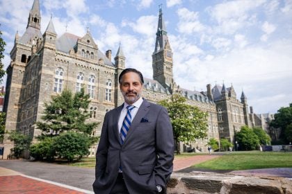 Eduardo Peñalver stands in a suit in front of the stone towers of Healy Hall