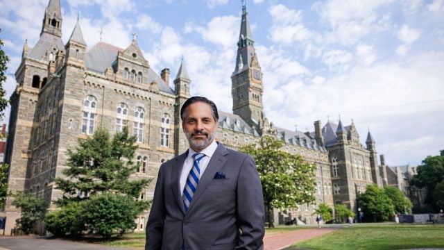 Eduardo Peñalver stands in a suit in front of the stone towers of Healy Hall