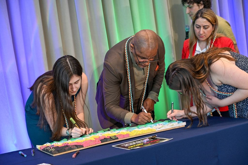 A group of people decorate a piece of art with markers on a table