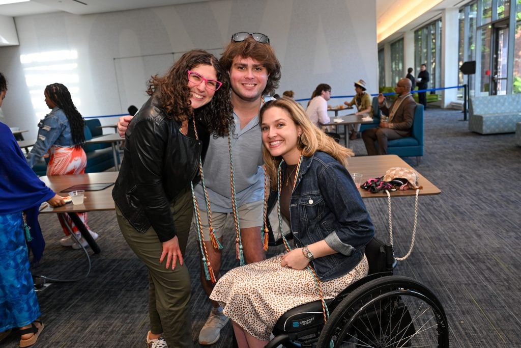 A young man with two young women, one of whom is in a wheelchair, with graduation cords draped around them