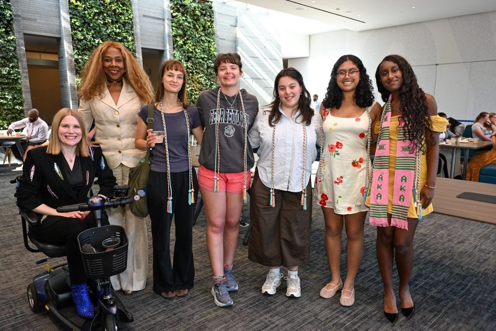 A group of women smiling with four young women with graduation chords