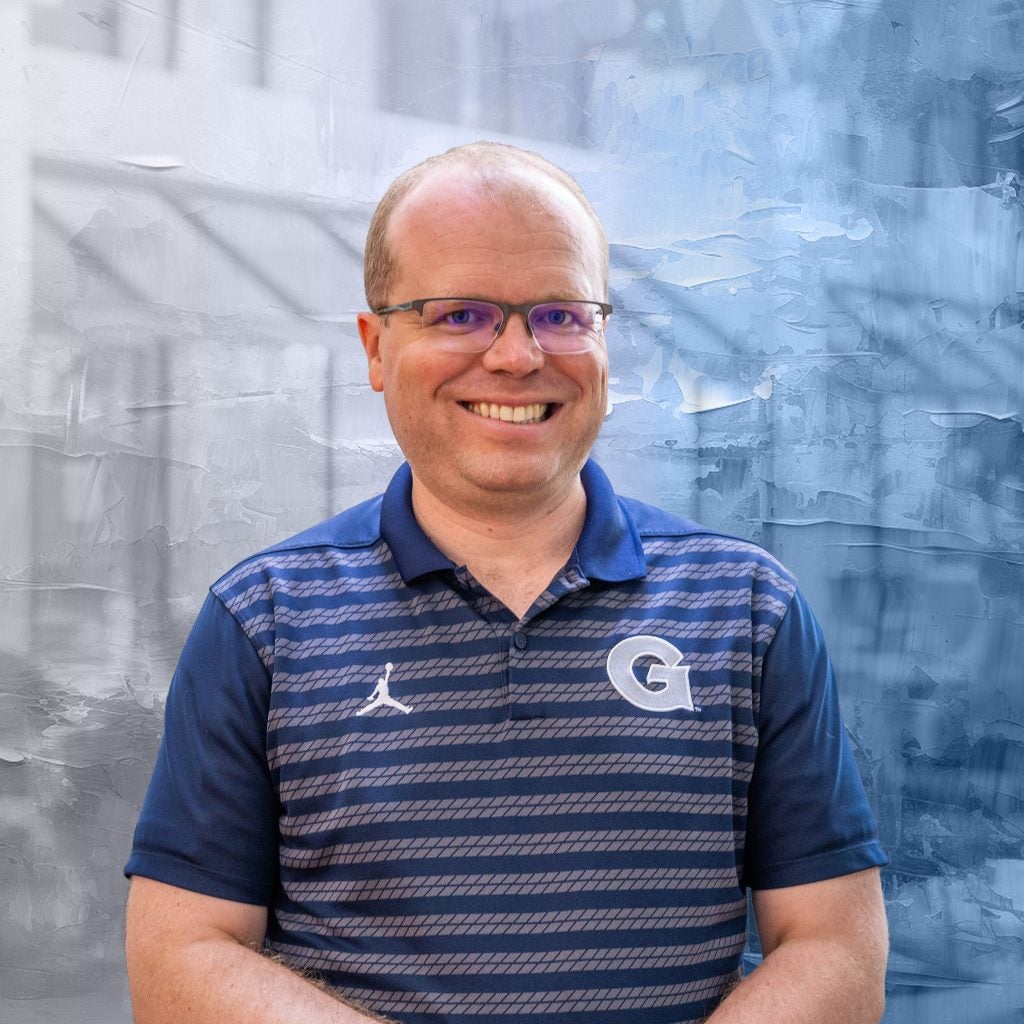 Caucasian man with glasses in blue Georgetown shirt smiling