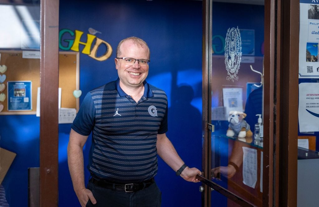 Caucasian man with glasses in blue Georgetown shirt smiling while opening door