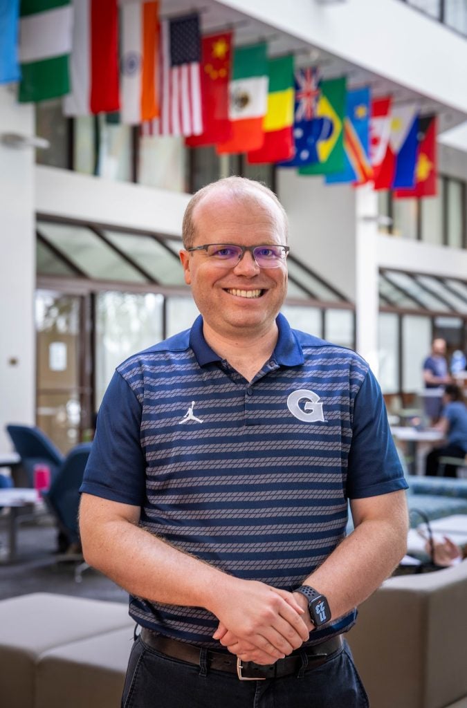 Caucasian man with glasses in blue Georgetown shirt smiling