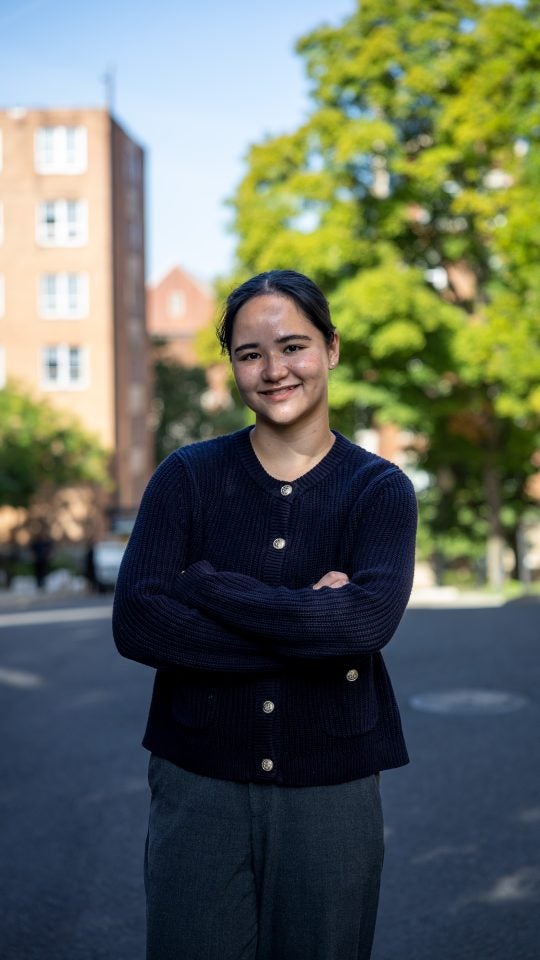 Young Asian woman with arms crossed smiling outside in blue sweater