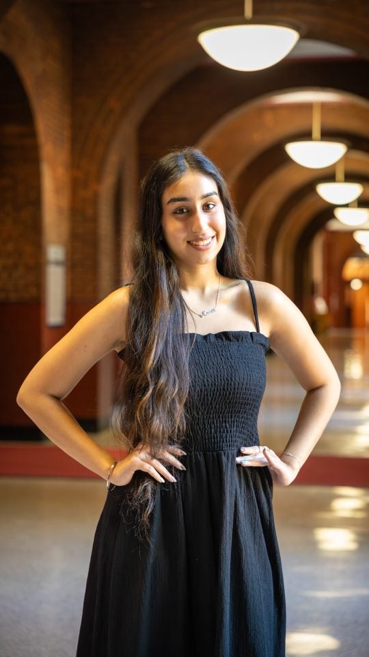Young woman in black dress with hands on hips smiling in Healy hallway