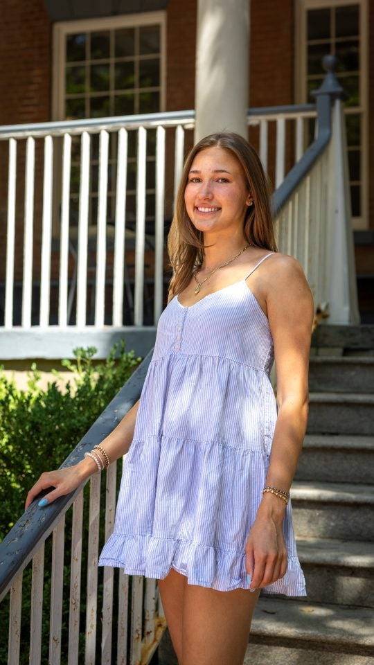 Young Caucasian woman in blue dress smiling with hand on staircase outside of Old North