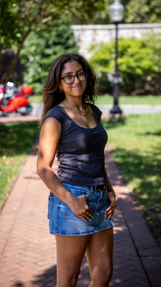 Young woman with glasses and blue shirt smiling while on a red brick pathway
