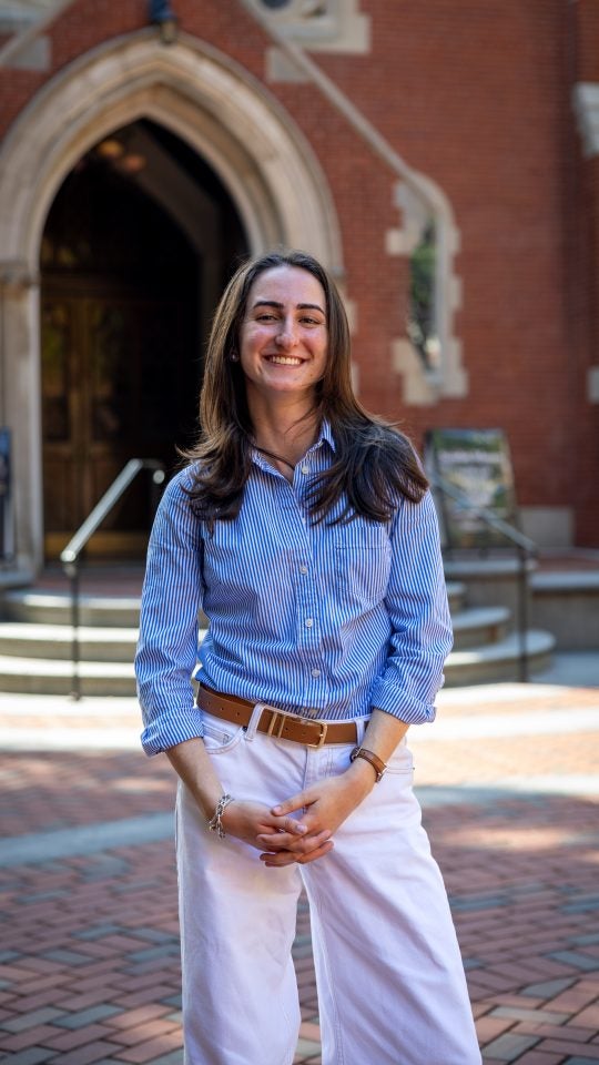 Young Caucasian woman in blue shirt in front of Dahlgren on a sunny day smiling