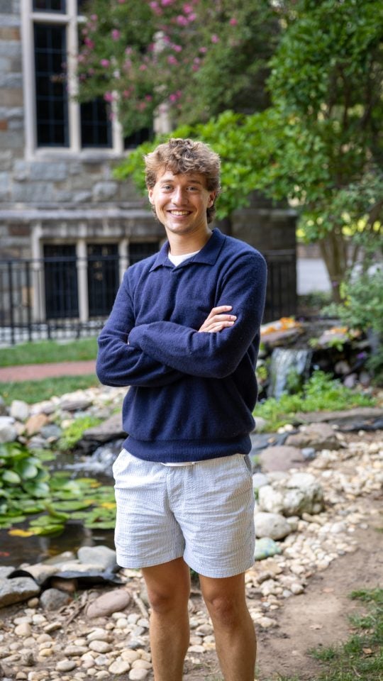 Young Caucasian man standing by koi pond smiling with arms crossed