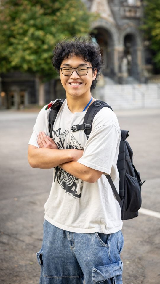 Young Asian man with glasses in a white graphic tee with arms crossed and smiling