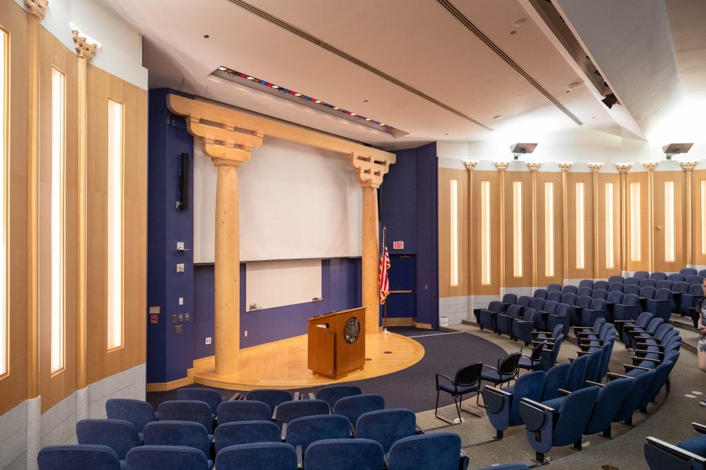 An auditorium at Georgetown with blue seats and wooden pillars onstage