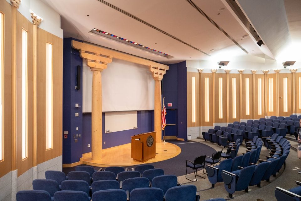 An auditorium at Georgetown with blue seats and wooden pillars onstage