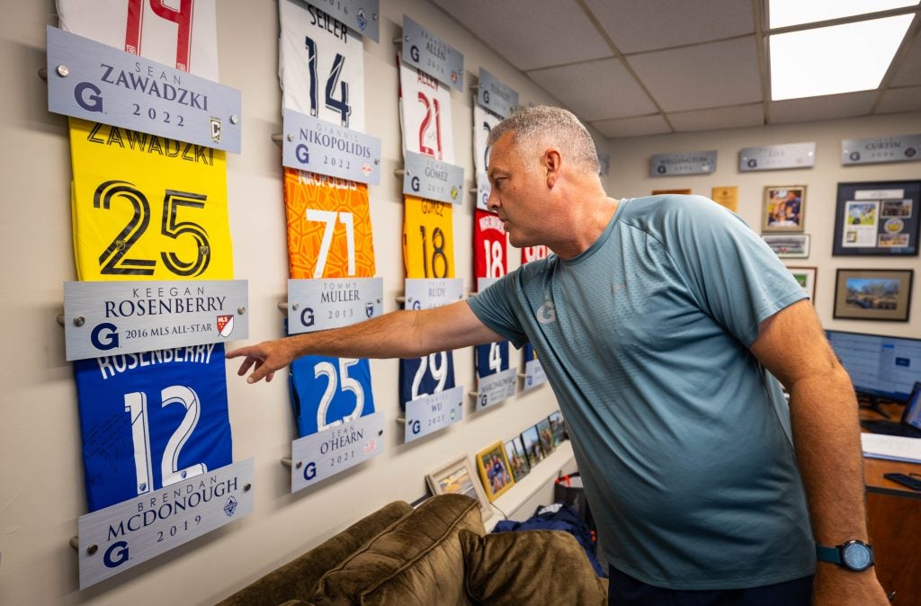 A coach points to a wall of soccer jerseys