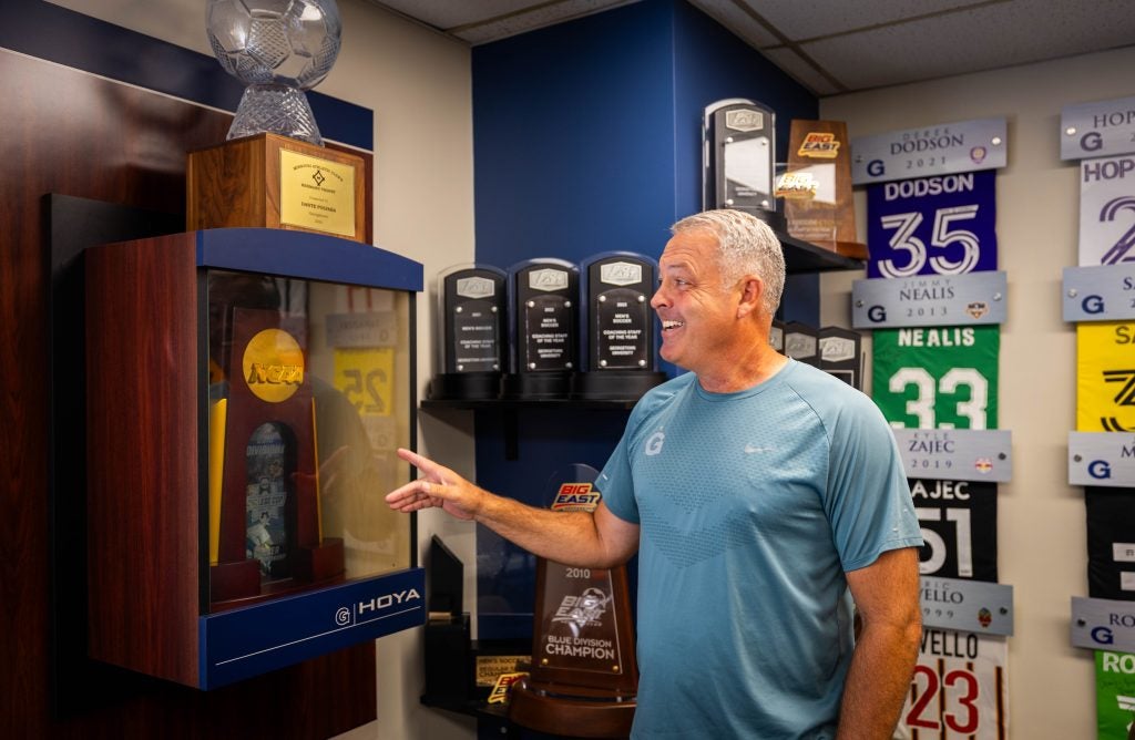 A coach smiles as he looks at a large trophy case