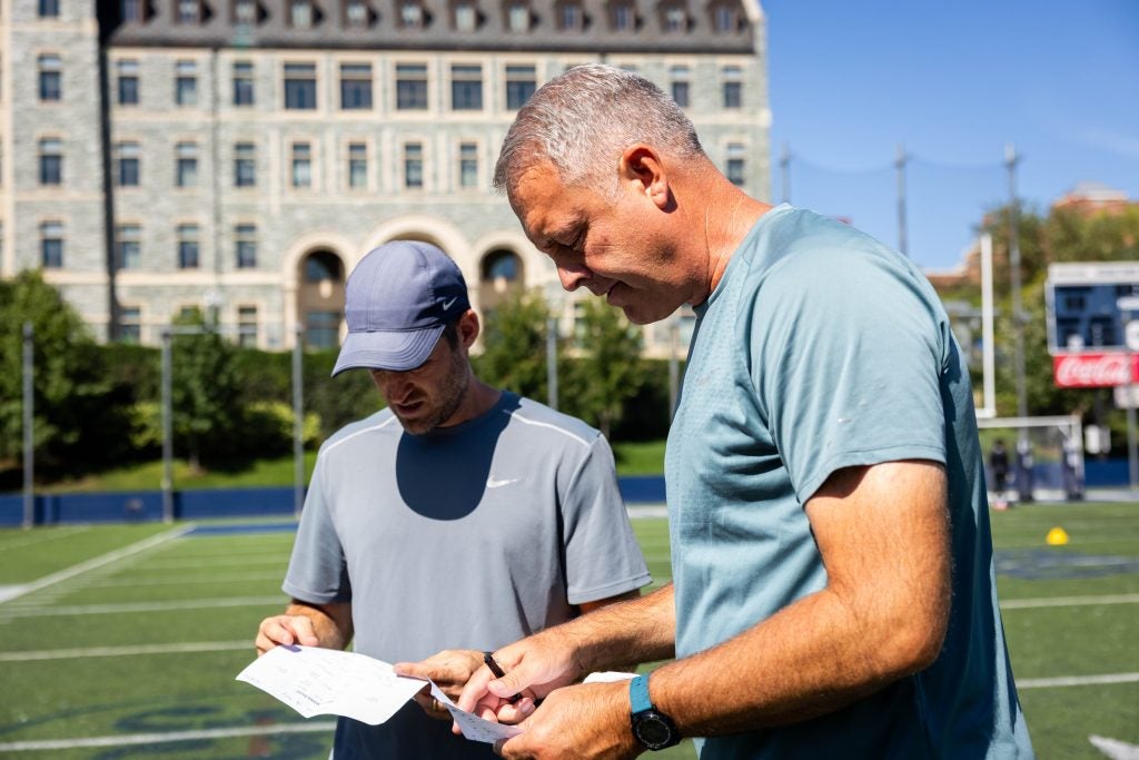 Two coaches looking at a piece of paper on a sunny day on a field
