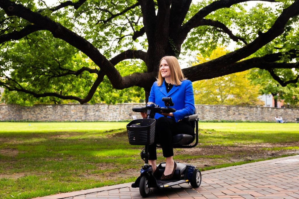 A woman on a mobility scooter smiles beneath a giant, expansive tree