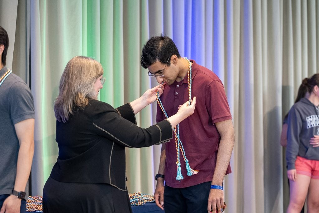 A woman drapes a graduation cord over a young man