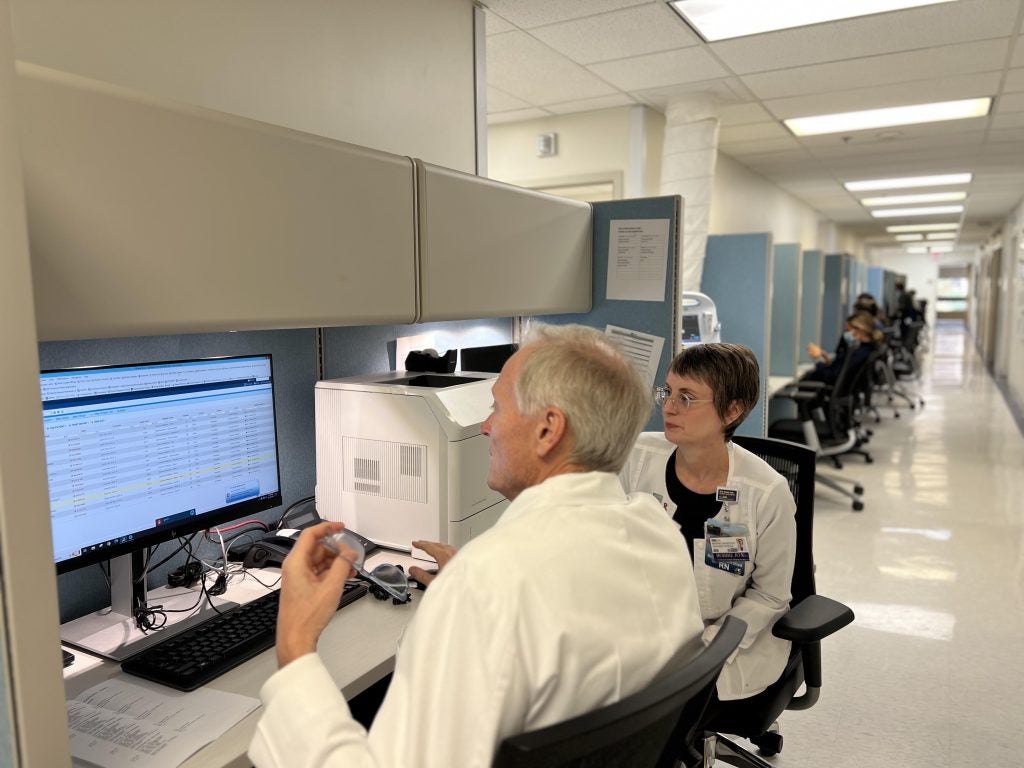Two people in white coats look at a computer together