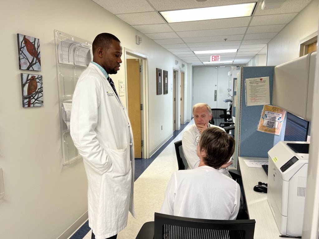 Three people in white coats talk in a medical setting