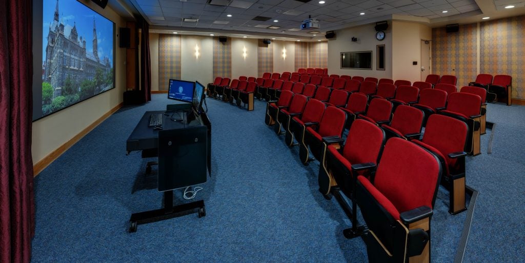 A rendering of a low-lit film screening room with red chairs