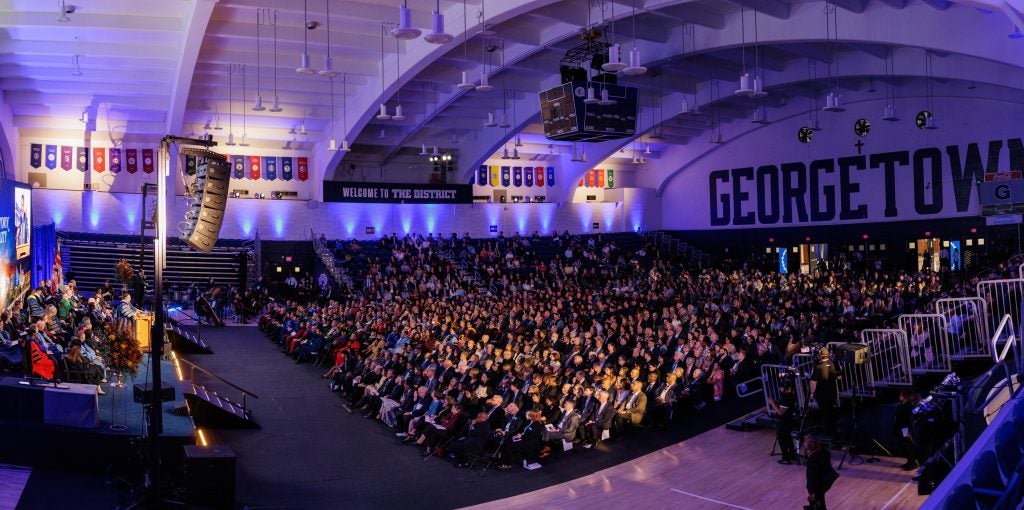 A crowd of audience members seated in an auditorium with the words "Georgetown" painted in all-caps behind them