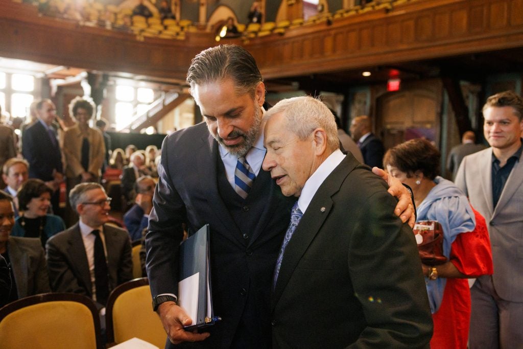 President Peñalver hugs his father in Gaston Hall. Both are wearing black suits
