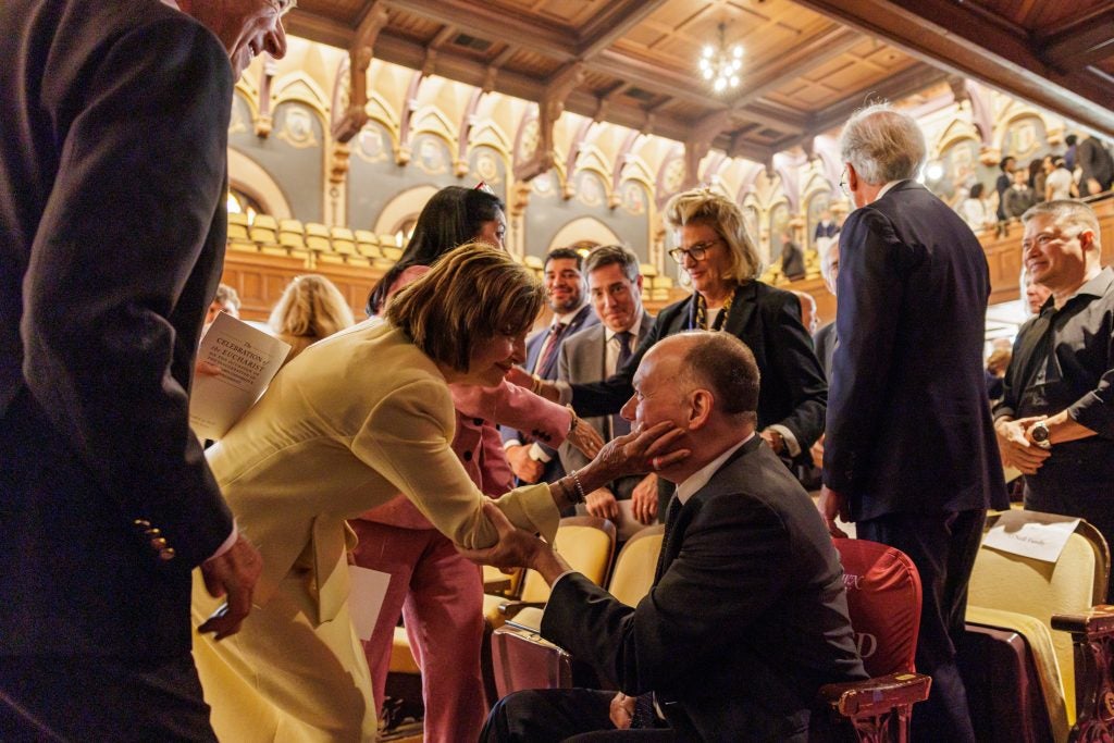 Speaker Emerita Nancy Pelosi, dressed in a yellow suit, greets former President John J. DeGioia in Gaston Hall