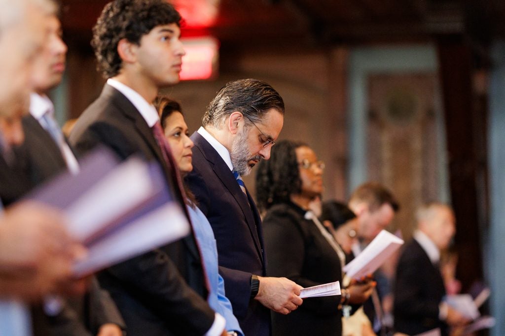 President Peñalver looks at a program book while singing a hymn during a Mass