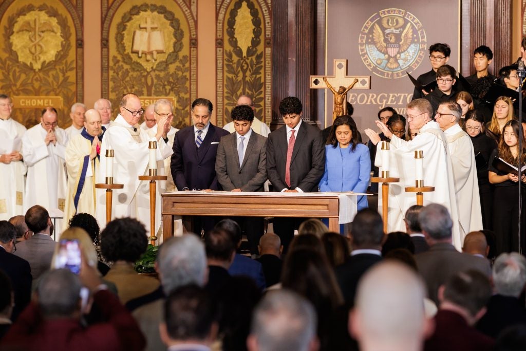 A family is blessed while standing onstage. Priests pray over them