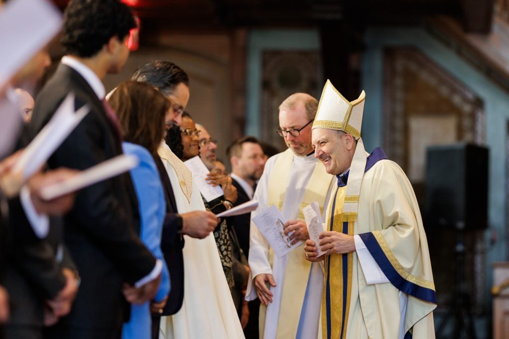 A bishop in a tall hat greets guests after a Mass