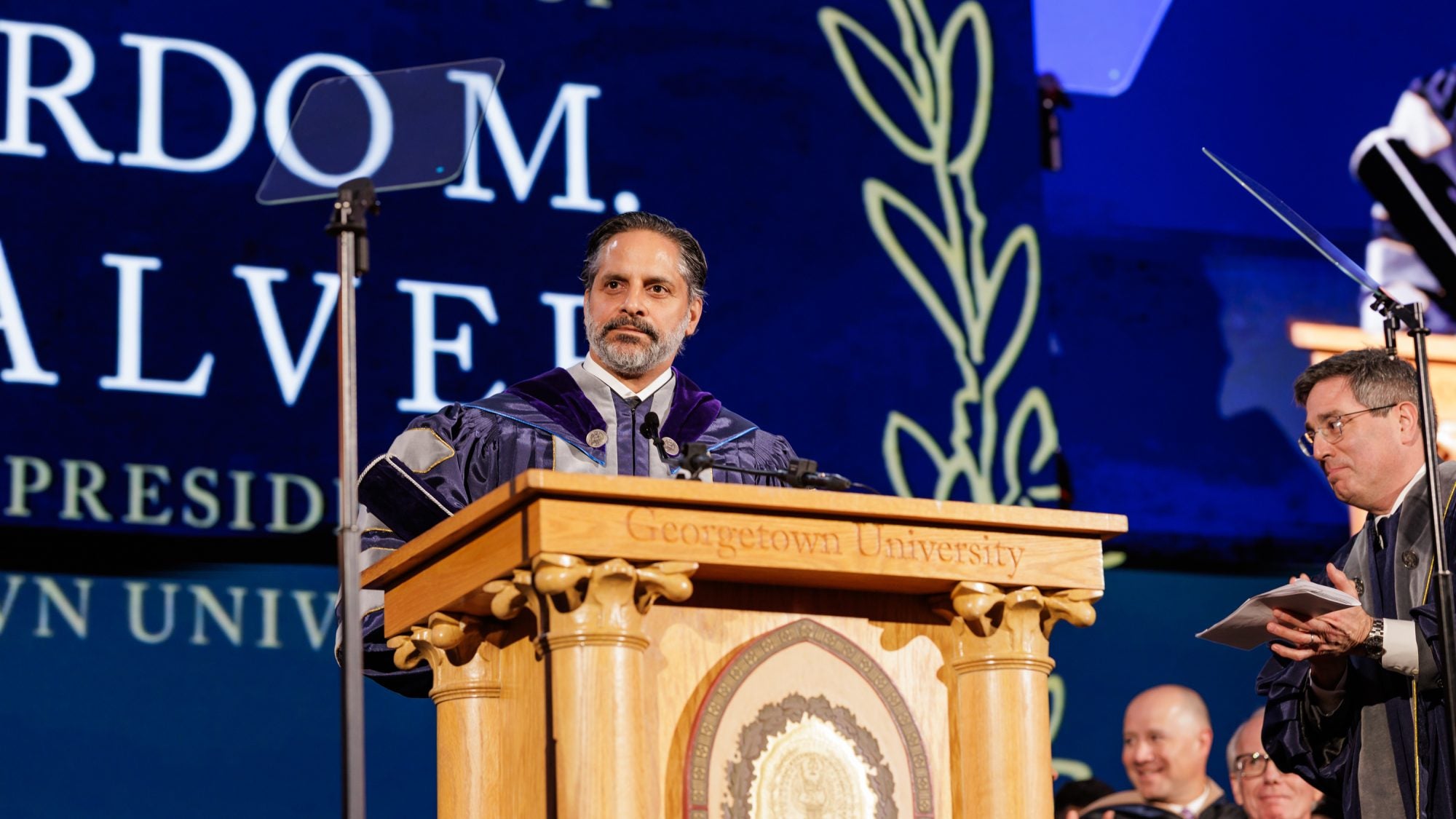 A president stands behind a podium in purple academic robes