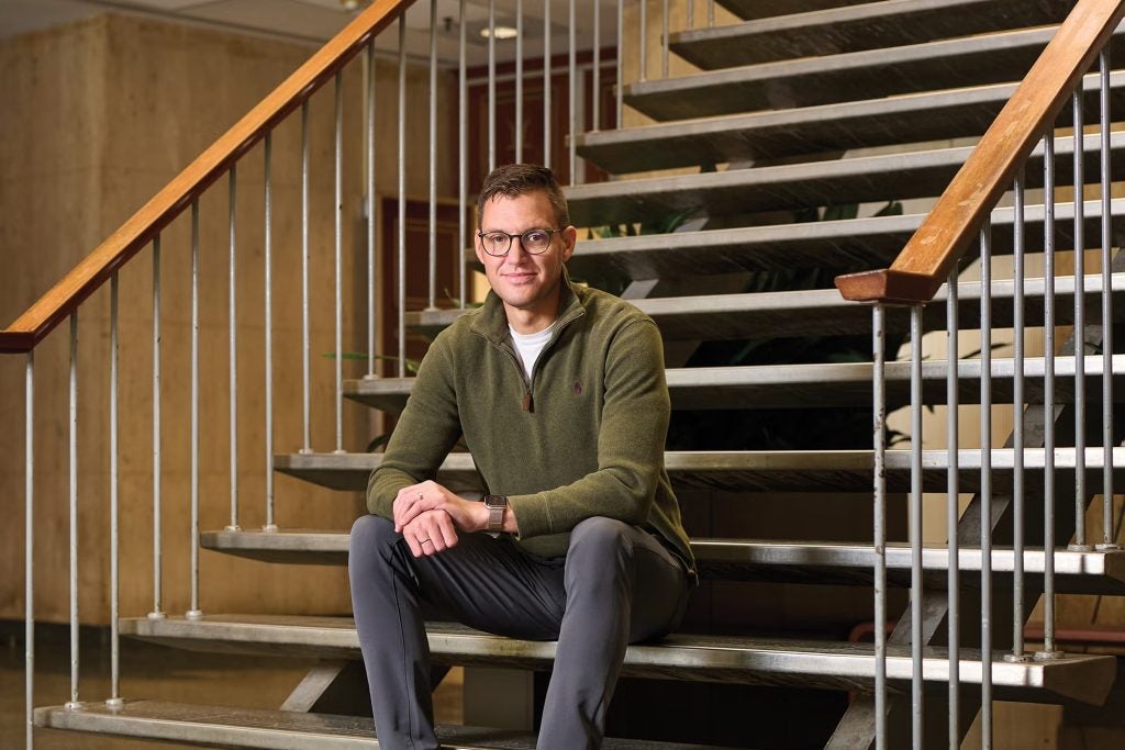 Man with glasses in green sweater sits on steps