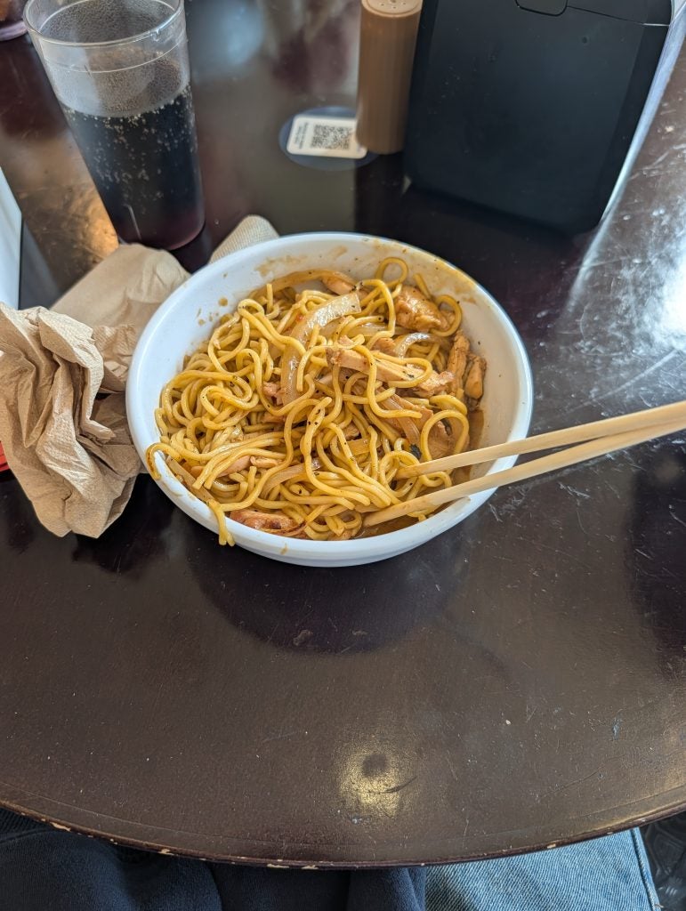 A white bowl with noodles and chopsticks