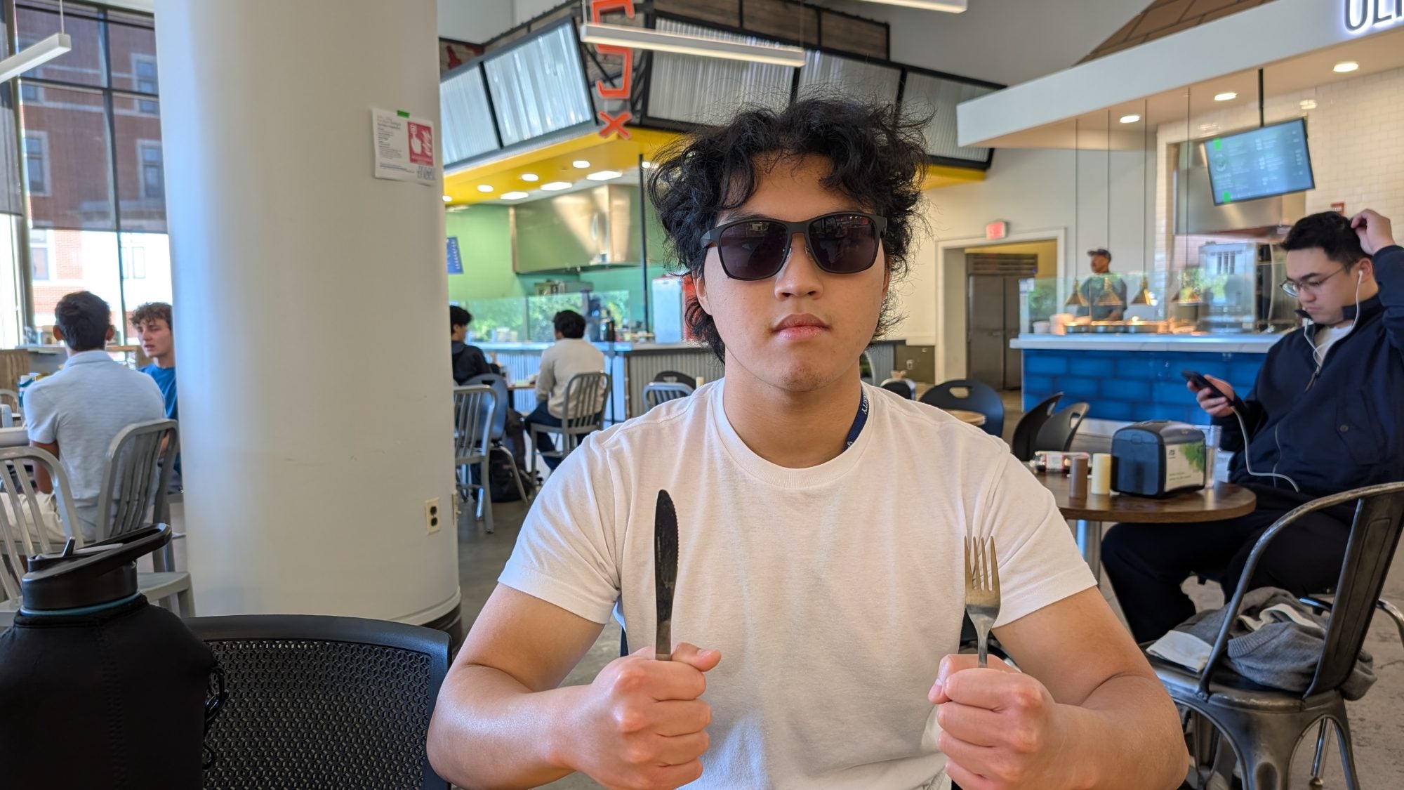 Young man with sunglasses at table holding fork and knife