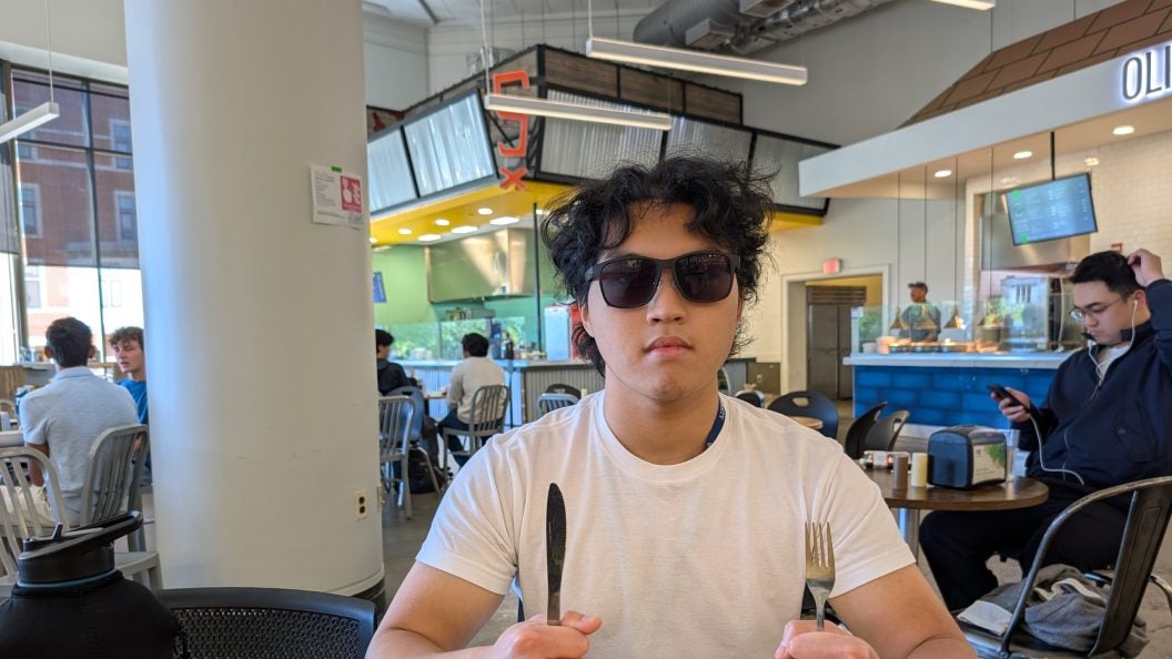 Young man with sunglasses at table holding fork and knife