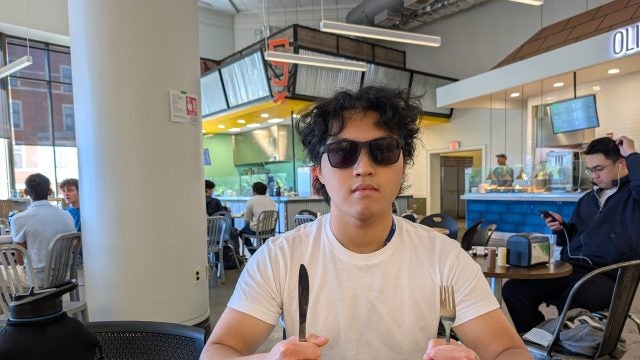 Young man with sunglasses at table holding fork and knife